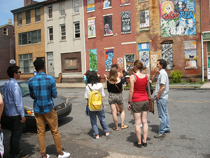 Students looking at a house wall painted with graffiti